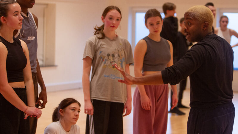 five dance students listening to advice given by the lead artist.