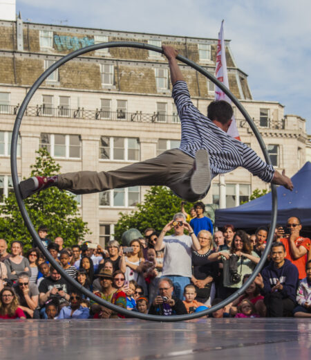 Man inside a human sized circus ring on a stage in front of a crowd.