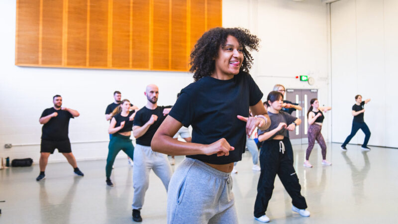 Class participants dancing and smiling in a studio.