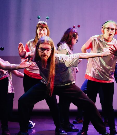 A mixed gender group of dancers performing on a purple lit stage