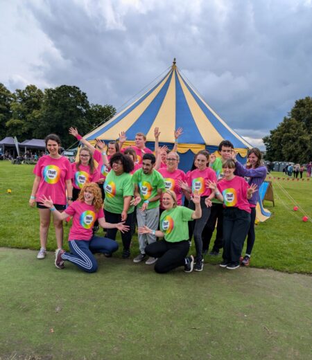 That! Dance Group dancers in colourful pink and green t-shirts posing in front of a striped tent
