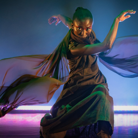 A dancer performing on stage whilst wearing a cape-like satin accessory that floats as they dance.