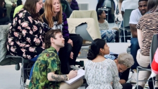 A group of diverse dance professionals and leaders listening to a session and writing notes