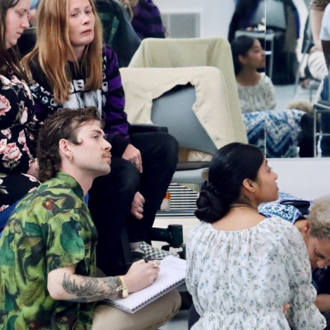 A group of diverse dance professionals and leaders listening to a session and writing notes