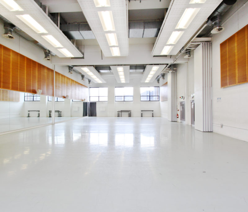 A brightly lit dance studio with large mirrored walls.