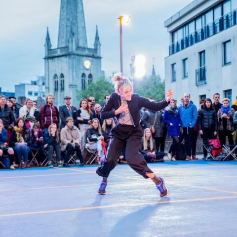 A street performer dancing who has drawn in a large crowd.