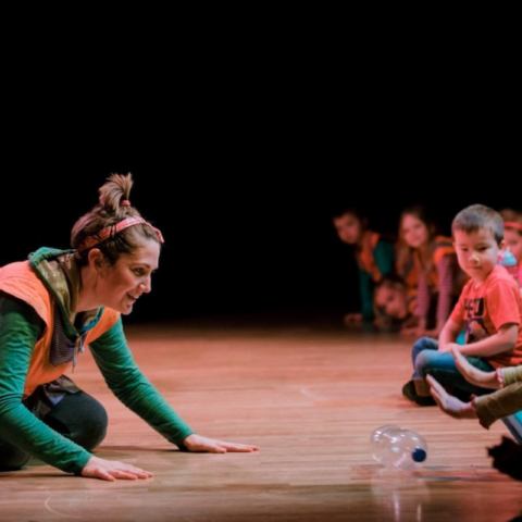 A performer sat on stage with an audience of children watching.